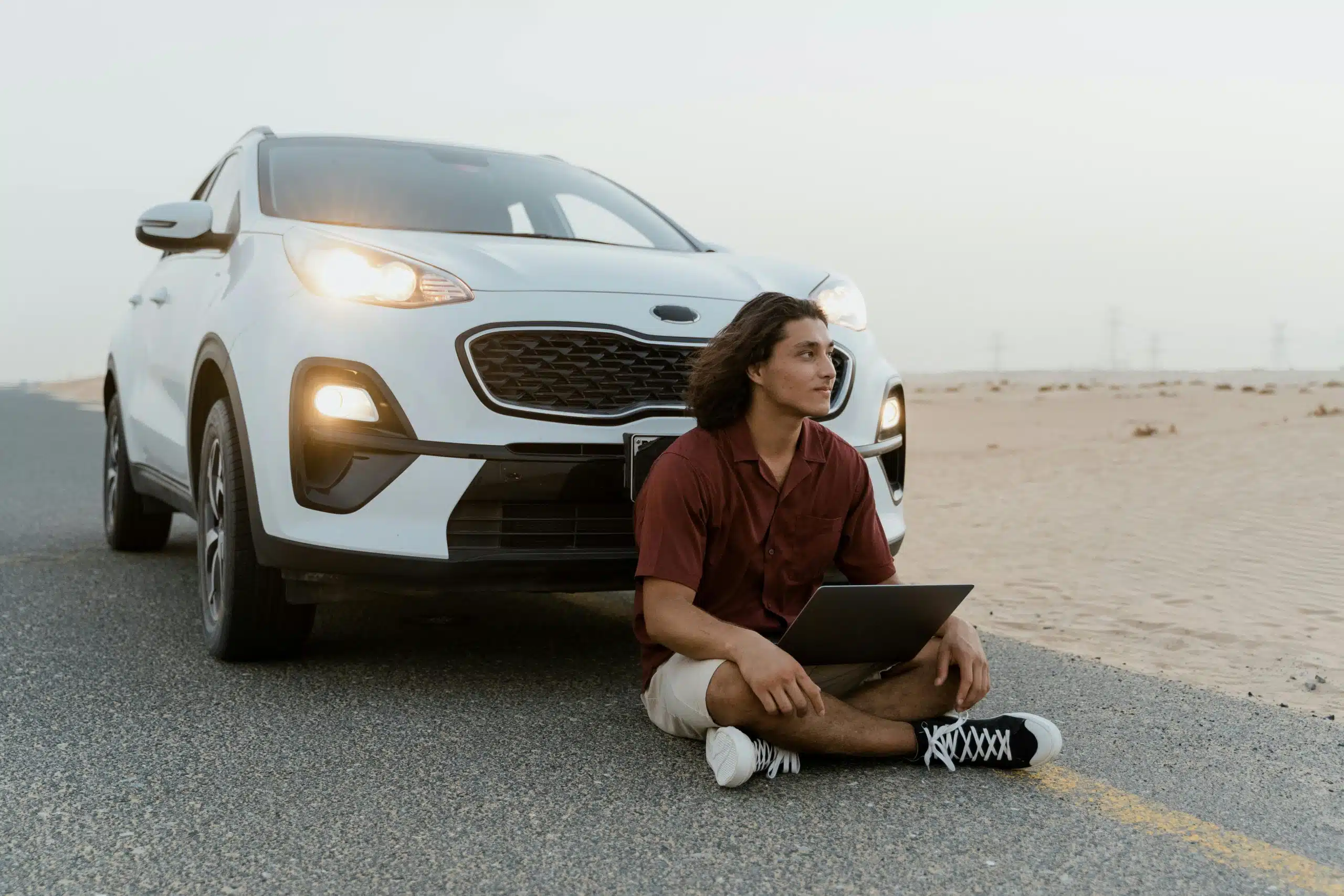 A man with a laptop sitting by an SUV on a desert road, working remotely.